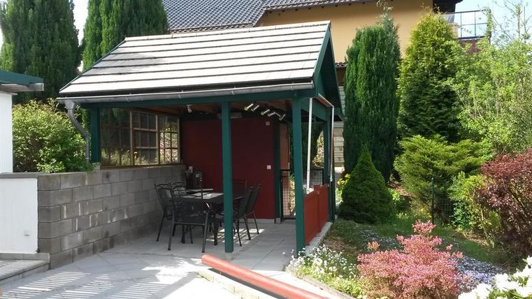Een mooie tuinpaviljoen met een tafel en stoelen. Omringd door groene planten en een goed onderhouden tuin.