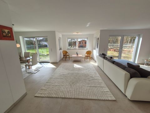 Eine helle und moderne Wohnräume mit großen Fenstern und einem gemütlichen Sofa. Der Raum ist mit einem Teppich und einfachen Möbeln eingerichtet.