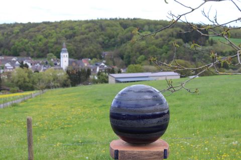Un paysage idyllique avec un grand lac et des forêts environnantes. Au premier plan, des champs et un bâtiment sont visibles.