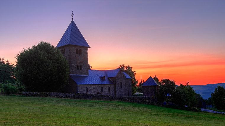 Une église au coucher du soleil avec une tour et des arbres au premier plan.