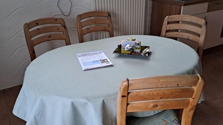 A round table with a bright tablecloth stands in a room. Around it, four wooden chairs are arranged.