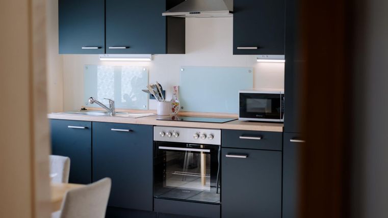 A modern kitchen with dark blue cabinets and stainless steel appliances. The room is bright and inviting, with a clear design.