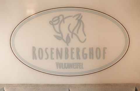 Ein Schild mit dem Schriftzug "ROSENBERGHOF" und der Zusatz "VulkanEifel". Das Design zeigt eine stilisierte Darstellung eines Tieres.