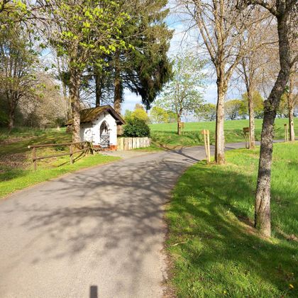 Een schilderachtige weg die door een groene landschap loopt. Langs de weg staat een klein, traditioneel huisje, omringd door bomen.