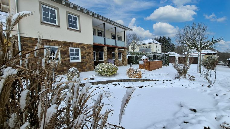 Ein hübsches Haus mit einem Garten, der mit Schnee bedeckt ist. Der Himmel ist klar und es gibt einige Wolken.