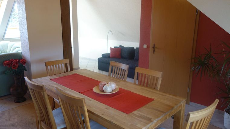 A cozy dining area with a wooden table and chairs. In the background, there is a gray couch and a plant arrangement.