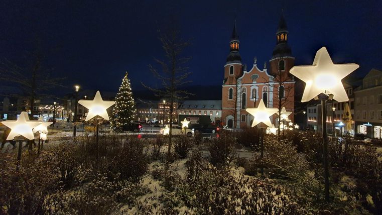 Een feestelijke scène met heldere sterren en een kerstboom. Op de achtergrond is een historische kerk 's nachts te zien.