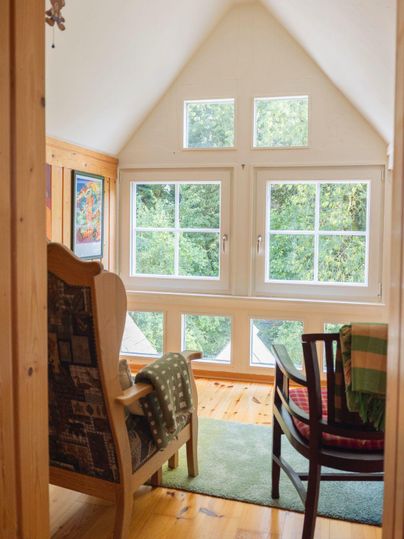 Une pièce confortable avec un fauteuil et une chaise. De grandes fenêtres offrent une vue sur l'extérieur verdoyant.