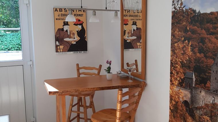 Eine kleine, gemütliche Ecke mit einem Holztisch und zwei Stühlen. An der Wand hängen nostalgische Plakate und über dem Tisch stehen Getränke.