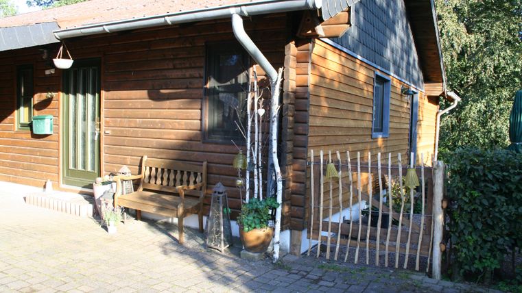 Een gezellig houten huis met een veranda en een bank. De entree is omringd door een kleine tuin.