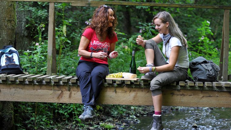 Zwei Frauen sitzen auf einer Brücke und legen bei der Wanderung eine Pause ein. 