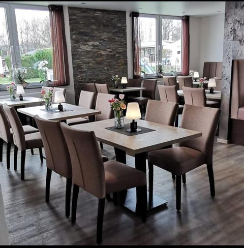 Een modern restaurant met meerdere tafels en elegante stoelen. De sfeer is helder en uitnodigend, met bloemstukken op de tafels.