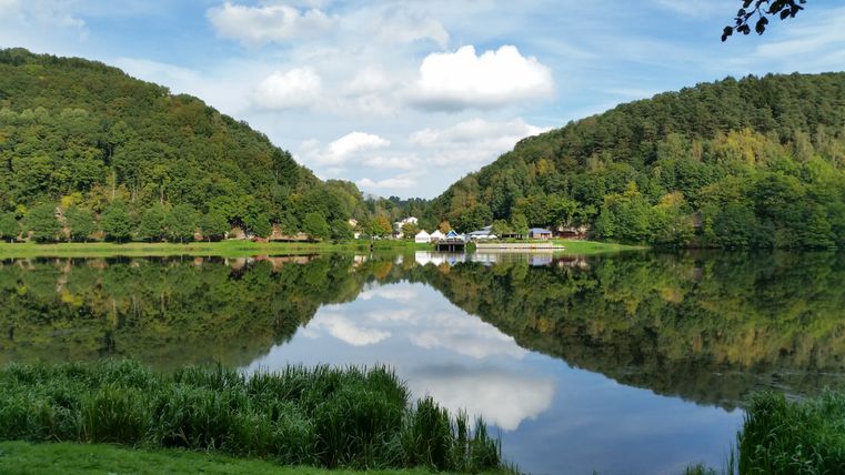 Panorama du lac de barrage de Bitburg avec des collines boisées et un reflet dans l'eau.