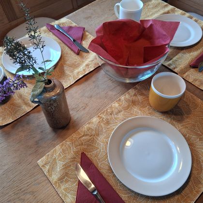 Een gedekte tafel met witte borden, kleurrijke kopjes en decoratieve servetten. In het midden staat een kom en een vaasje met bloemen.