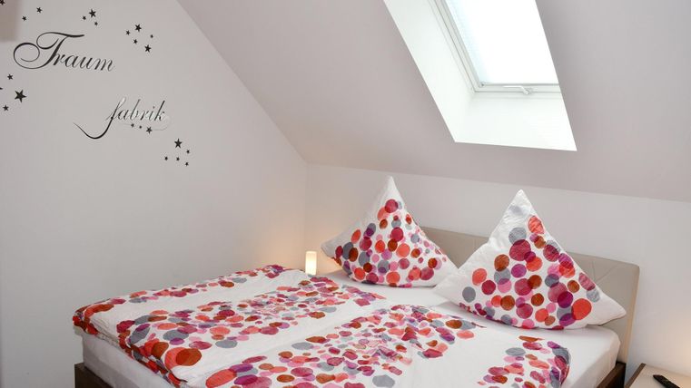 A cozy bedroom with a double bed and colorful cushions. On the wall is the inscription "Dream Factory".