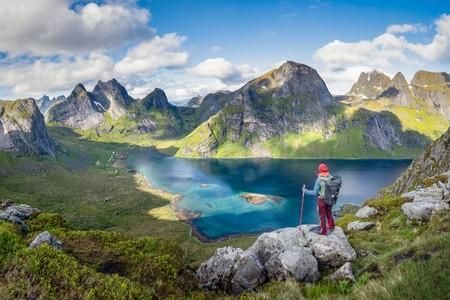Ein Wanderer steht auf einem Felsen und blickt auf eine malerische Landschaft mit Bergen und einem klaren See. Die Aussicht ist beeindruckend und vermittelt das Gefühl von Freiheit in der Natur.