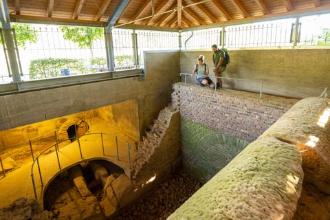 Two people look at an ancient Roman well room in a covered area.