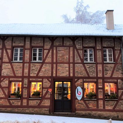 Ein altes Fachwerkhaus mit roter und brauner Fassade. Vor dem Gebäude liegt Schnee, und die Fenster sind warm beleuchtet.