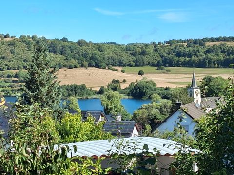 A picturesque view of a green landscape with fields and a body of water. In the background, a village and a church can be seen.