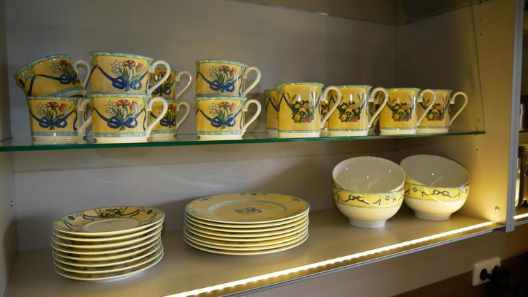 Een rek met kleurrijk servies. Boven staan er kopjes met bloemmotieven en beneden borden en kommen.