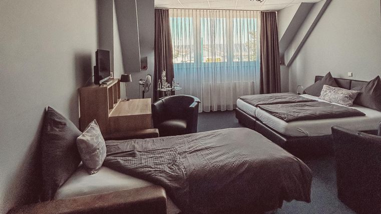 Une chambre d'hôtel moderne avec deux lits et un bureau. De grandes fenêtres laissent entrer beaucoup de lumière et la pièce est décorée de manière épurée.