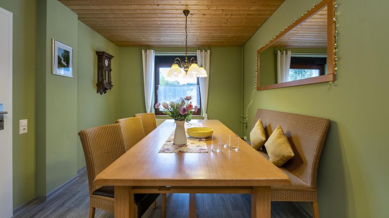 Een gezellige eetruimte met een grote houten tafel en stijlvolle stoelen. De muren zijn in een zachte groentint geschilderd en er is een warm verlichte plafondlamp.