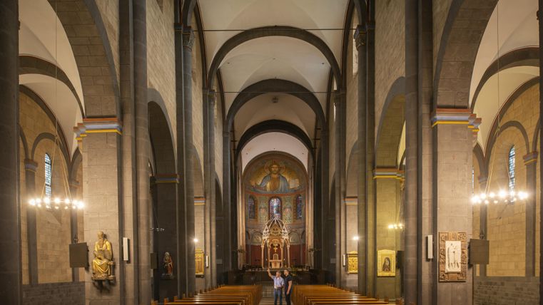 Un intérieur d'église impressionnant avec de voûtes hautes et des rangées de bancs en bois. À l'arrière-plan se trouve un retable artistique.