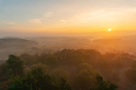 Sonnenaufgang über nebligen Hügeln und bewaldeter Landschaft