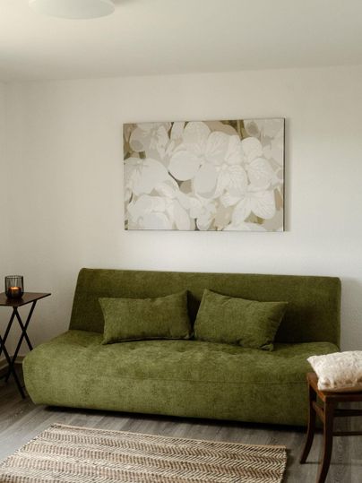 Un salon élégant avec un canapé vert et une peinture moderne sur le mur. Un tapis neutre et une petite table complètent l'atmosphère accueillante.