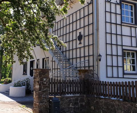 Un bâtiment charmant avec une façade lumineuse et un bel escalier. Au premier plan, il y a un mur en pierre et un jardin bien entretenu.