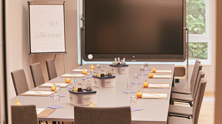 Een moderne vergaderruimte met een lange tafel en stoelen. Op de tafel staan waterkaraffen en kleine decoraties.