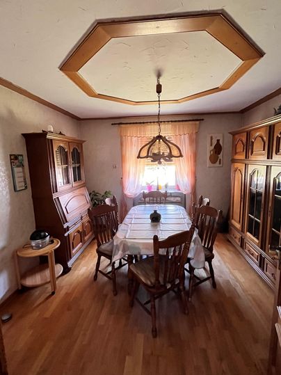 A cozy dining area with a large wooden table and several chairs. A window with curtains allows for natural light and creates a warm atmosphere.