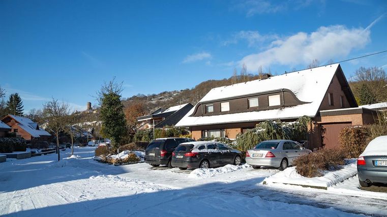 Een rustige straat in de winter met met sneeuw bedekte huizen en bomen. De lucht is helder en blauw.