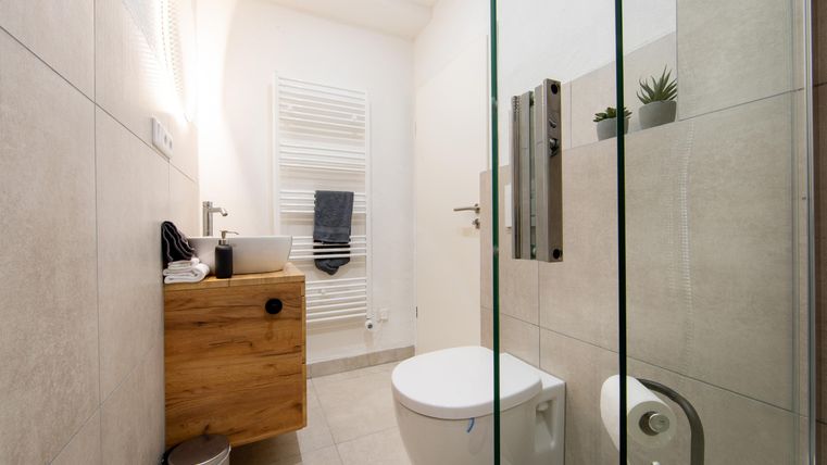 Ein modernes Badezimmer mit einer Glasdusche und hellen Fliesen. Eine Holzkommode ist neben dem Waschbecken platziert.