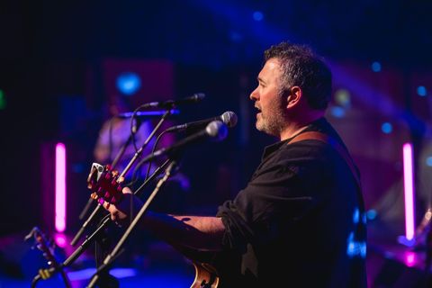 A musician is playing guitar on a stage. Colorful lights create an atmospheric ambiance.
