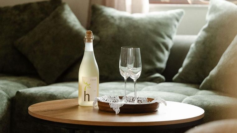 Une bouteille avec une boisson se trouve sur une table en bois. À côté de la bouteille, deux verres élégants sont posés sur un plateau.