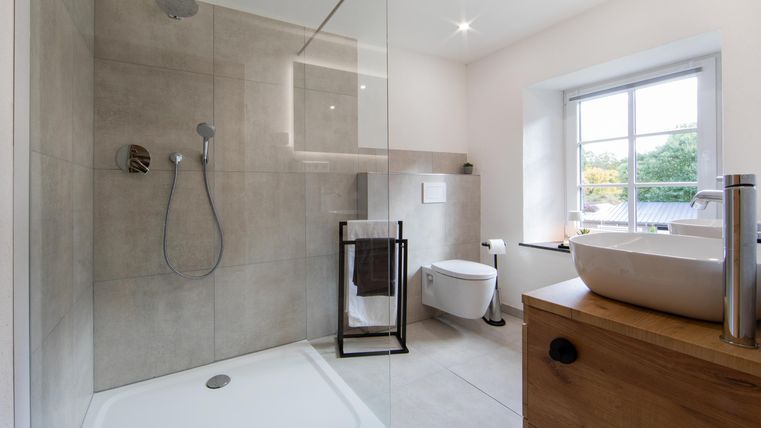 Ein modernes Badezimmer mit einer begehbaren Dusche und einem Waschbecken. Helle Wände und ein Fenster sorgen für viel Tageslicht.