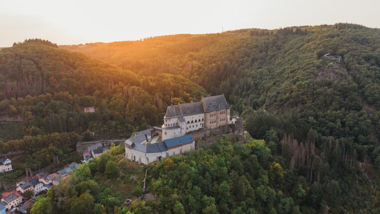 Vue aérienne du château de Vianden au Luxembourg au coucher du soleil, entouré de collines boisées.