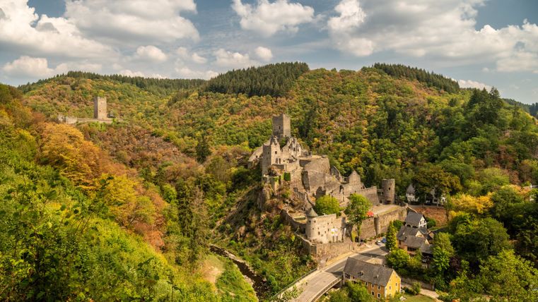 Landschaft mit Manderscheider Burgen im Herbst, umgeben von buntem Laub und bewölktem Himmel.