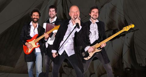 A band with four members is on stage.
They play different instruments and appear energetic and enthusiastic.