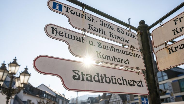Ein Wegweiser mit verschiedenen Richtungen und Informationen für Touristen. Im Hintergrund sind Gebäude und Stadtlichter sichtbar.