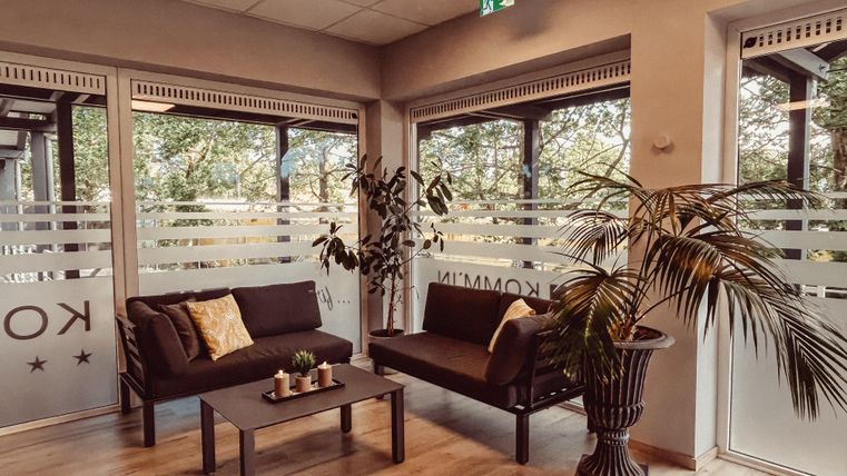 Een moderne wachtkamer met twee banken en een tafel. Grote ramen bieden uitzicht op de natuur en laten veel licht binnen.