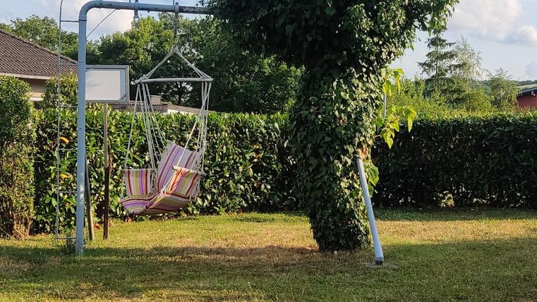 A garden with a hammock and a unique tree that has an interesting shape. The sky is blue with some clouds.