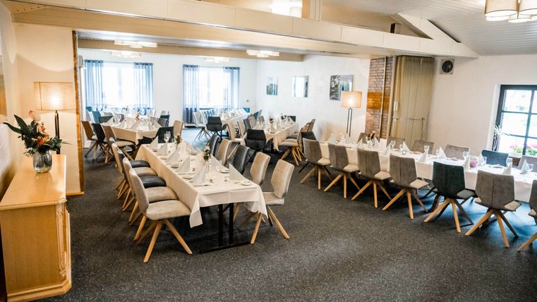 An elegant event space with covered tables and chairs. Soft lighting and large windows create an inviting atmosphere.