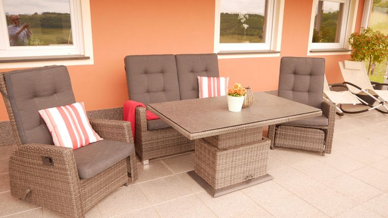 Een gezellige terrace met rieten meubels en comfortabele kussens. De tafel staat in het midden en een bloempot zorgt voor een uitnodigende sfeer.