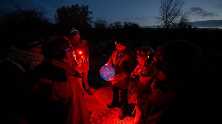 Eine Gruppe von Menschen steht im Dunkeln und hält leuchtende Laternen. Die Atmosphäre ist mystisch und festlich.