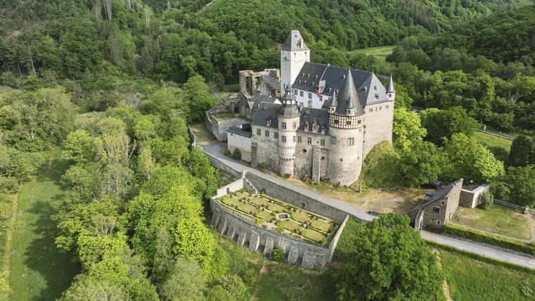 An impressive castle with towers and a beautiful garden surrounded by forest.