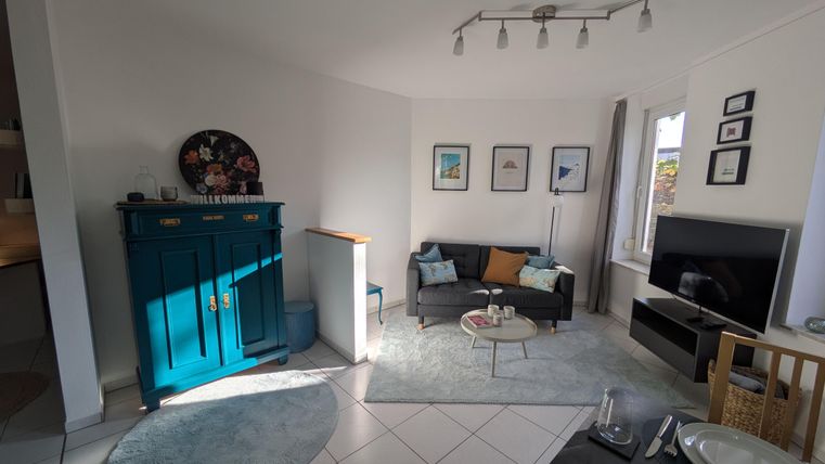 Een modern woonkamer met een blauwe kast, een bank en een tafel. De muren zijn versierd met foto's en er is veel daglicht.