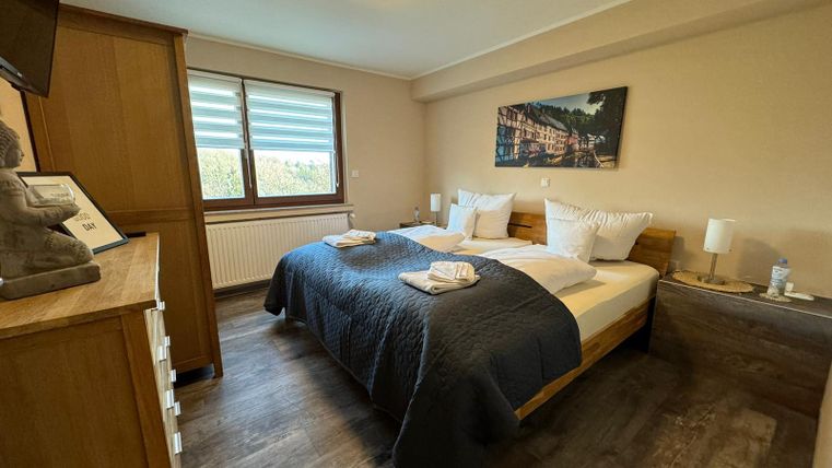 A cozy bedroom with a large bed and modern furniture. The walls are in soft colors and large windows let in plenty of light.