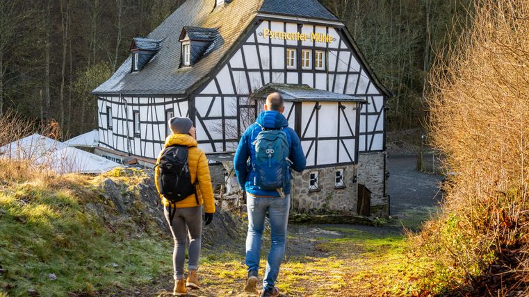 Two hikers in front of the Pyrmont Mill on a forest path.